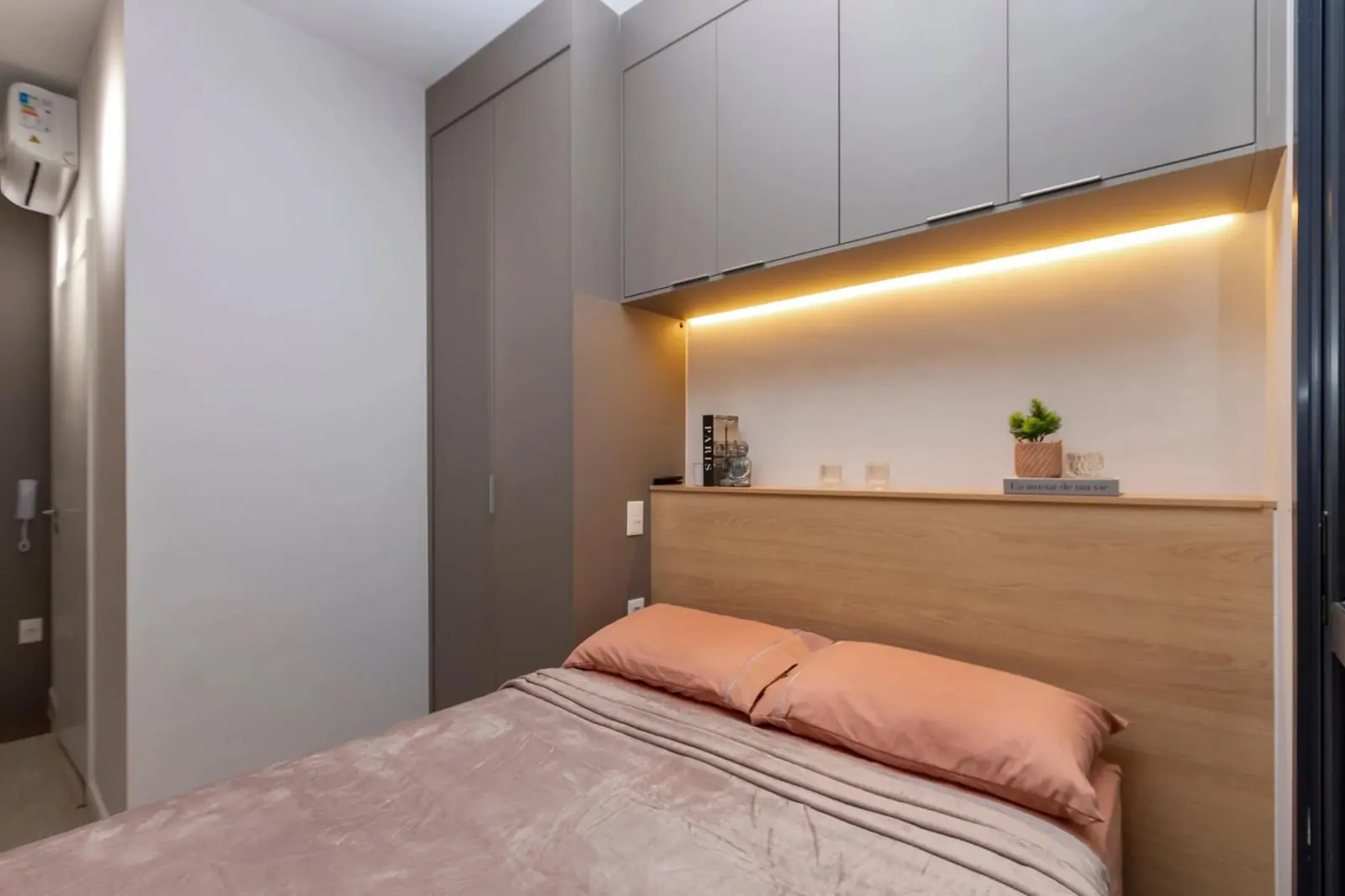 Cama de casal do Studio Ipê com cabeceira de madeira e armários com iluminação em LED