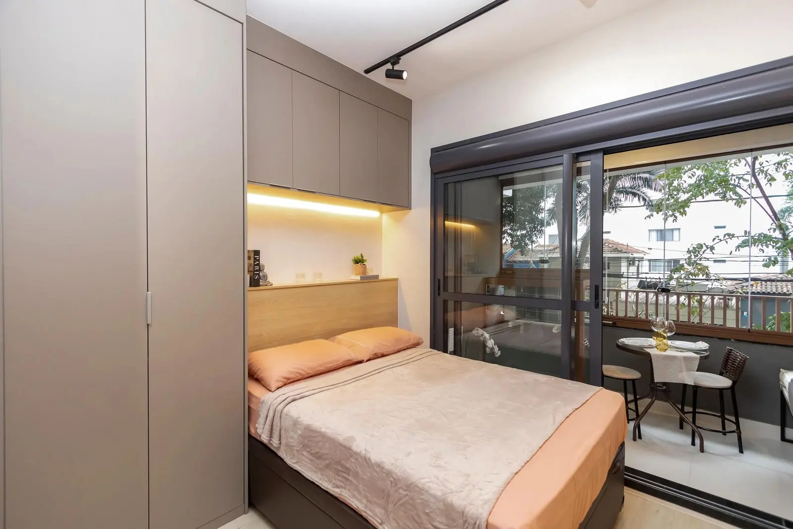 Cama de casal e sacada do Studio Ipê com vista para as árvores da rua