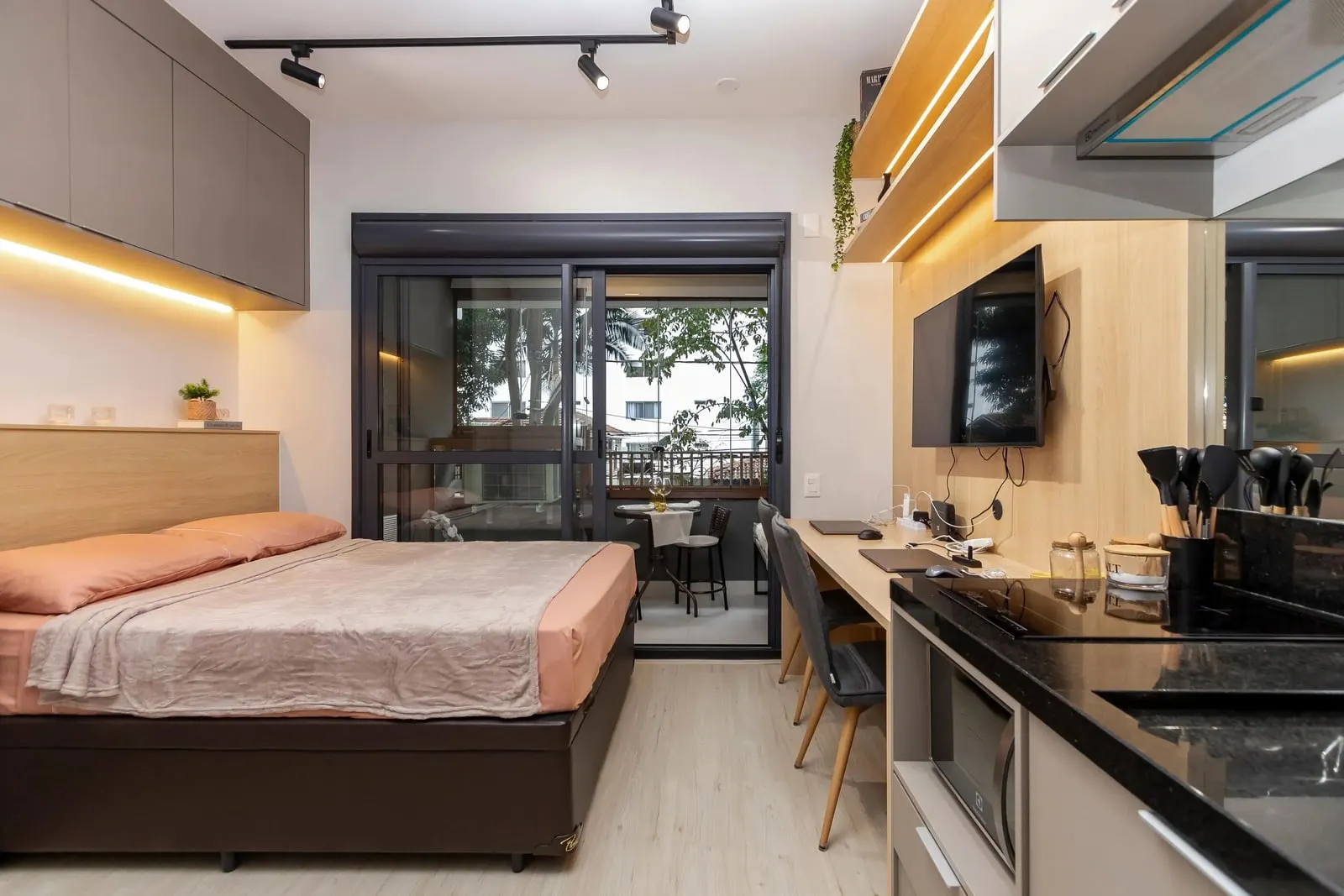 Vista ampla do Studio Ipê: cama de casal, cozinha equipada e sacada envidraçada no Haus Mitre Campo Belo