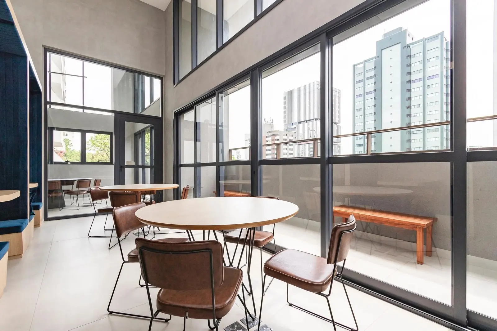 Coworking do Haus Mitre Campo Belo com mesas redondas e vista da cidade pelas janelas