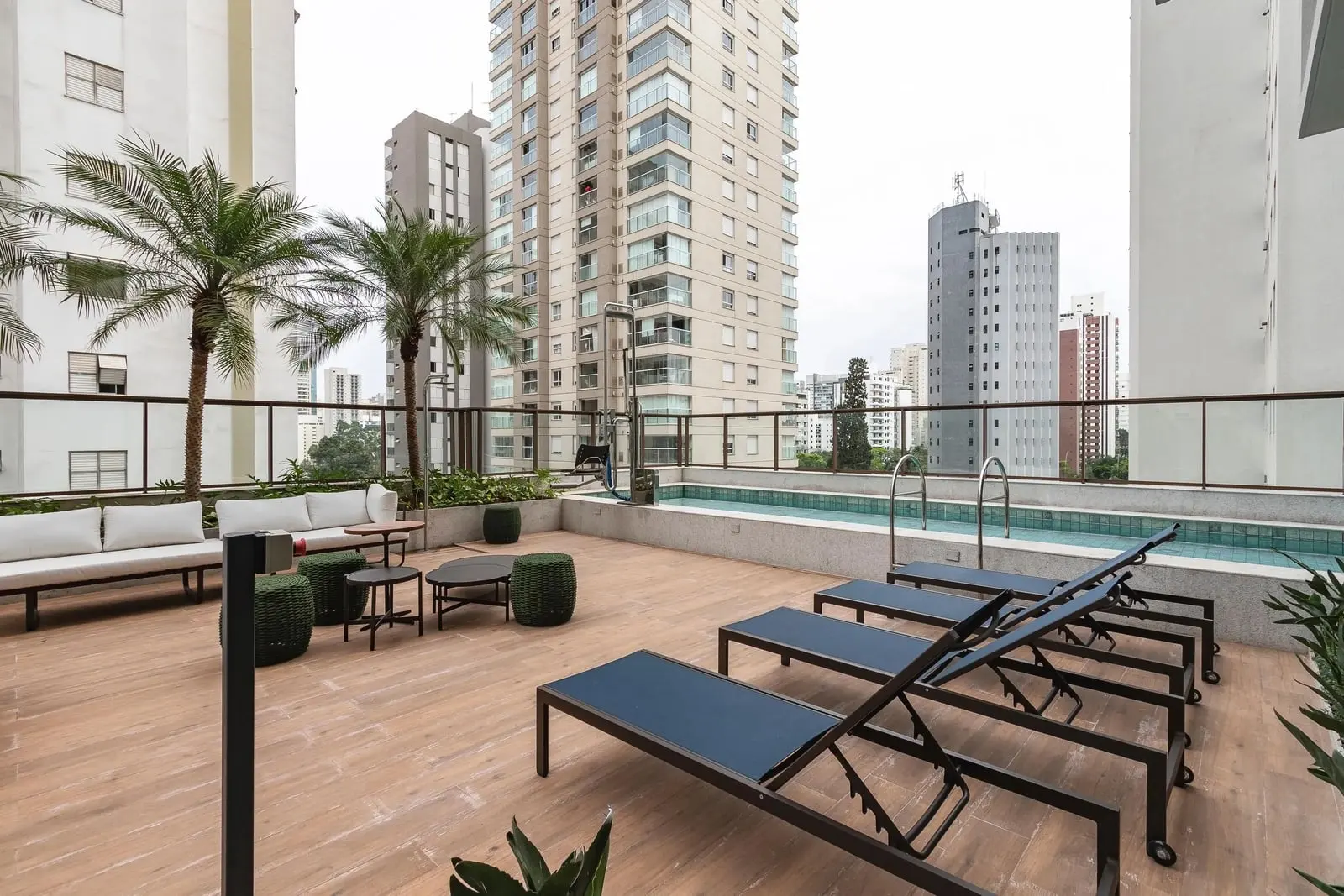 Deck da piscina do Haus Mitre Campo Belo com palmeiras, sofá e mesas de apoio