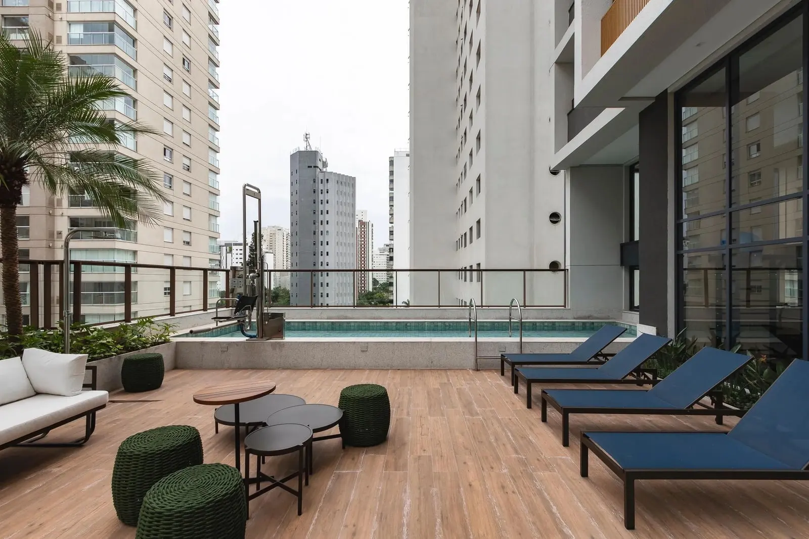 Piscina do Haus Mitre Campo Belo no 5º andar, com deck de madeira e espreguiçadeiras azuis